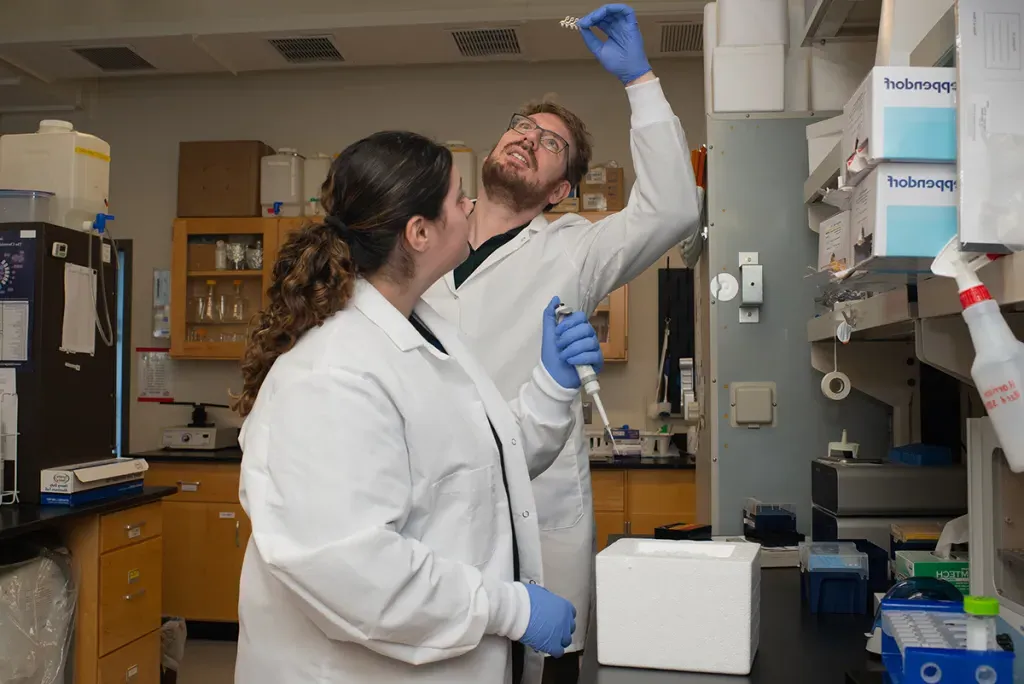 Two U N E students hold a slide up to the light