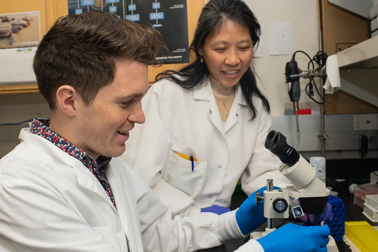 A research professor helps a student with a microscope